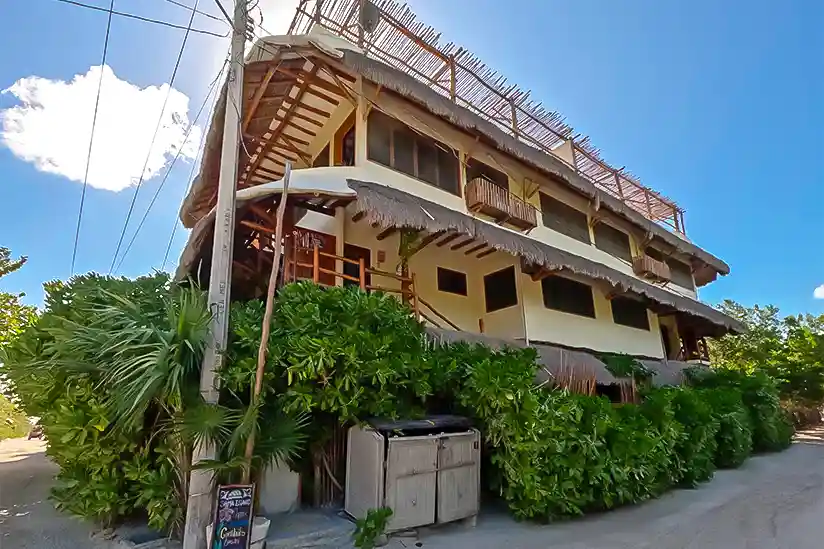 Das Gebäude der Holbox Deluxe Apartments umgeben von einem begrünten Zaun.