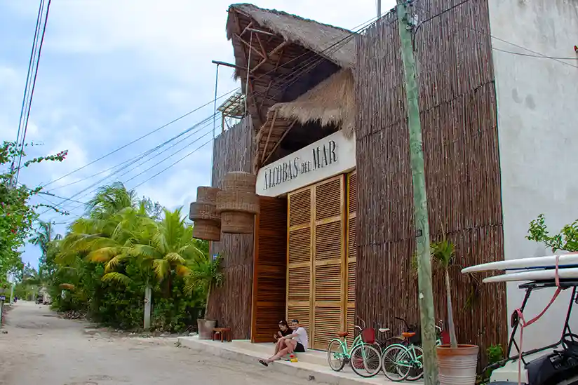The wooden entrance gate of the Holbox Hotel Alcobas del Mar surrounded by palm trees.