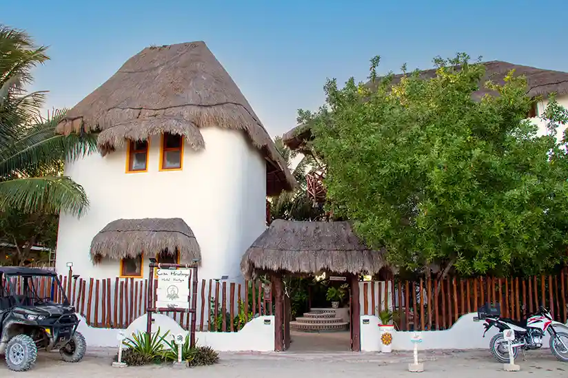 The white building of the Holbox boutique hotel Casa Hridaya with a thatched roof.