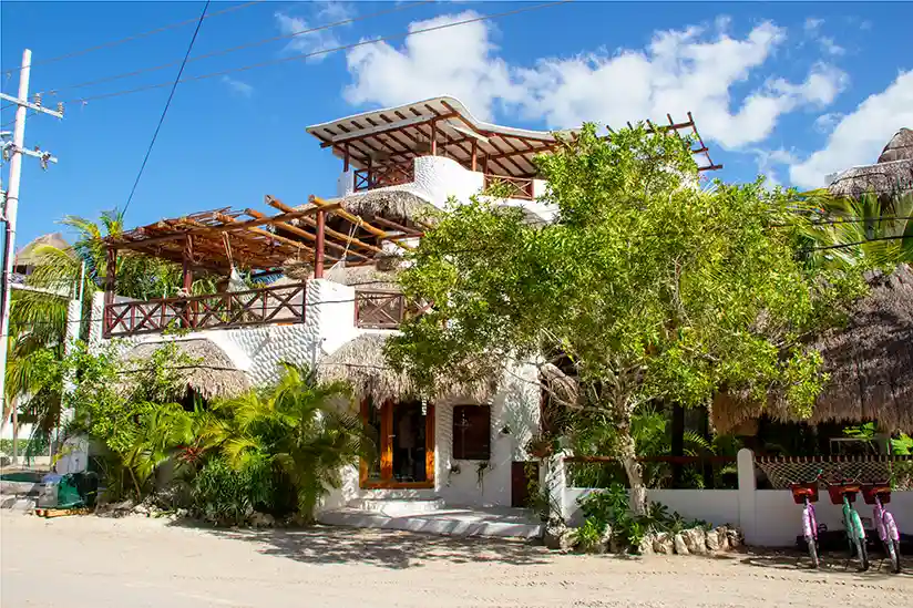 The white building is El Corazón Boutique Hotel in Holbox with palm trees in the entrance area.