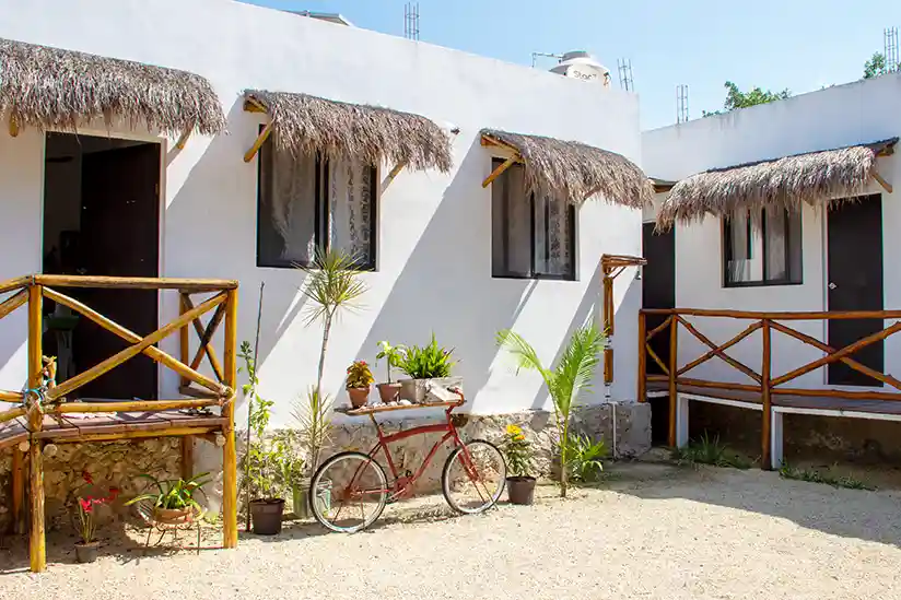 Hotel EncantaLuna Holbox, a white building with thatched roofs, surrounded by palm trees and tropical vegetation.