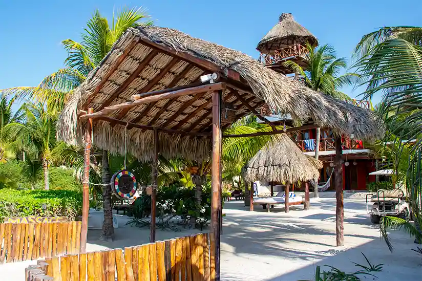 The thatched-roof entrance to the Holbox boutique hotel Palapas del Sol with a wooden tower in the background.