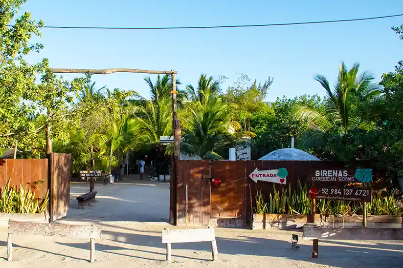 The entrance to the Holbox Hotel Sirenas Caribbean Rooms with a view of the garden with palm trees.