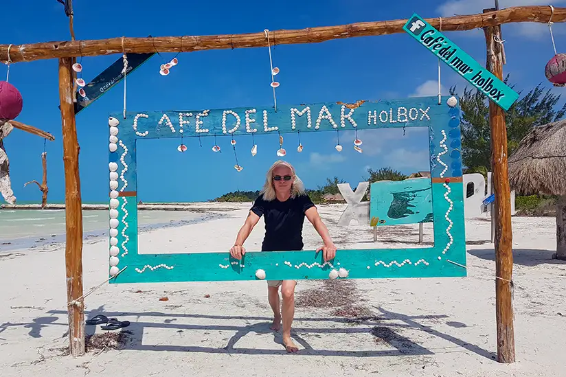 Christian from Isla Holbox Info standing on the beach in front of the iconic Café del Mar sign.