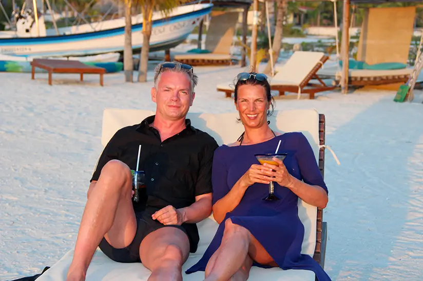 Isla Holbox Info founders Christian and Margit enjoying the sunset with cocktails on beach sun loungers.