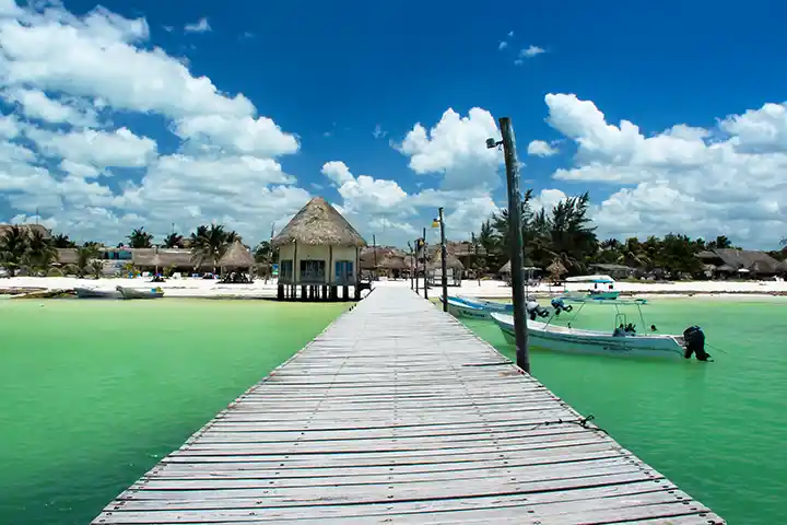Holzsteg am nördlichen Pier von Holbox mit Fischerbooten und Hütten im Hintergrund.