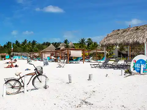 Beach club on Isla Holbox with deck chairs and a bicycle in the sand against a blue sky.