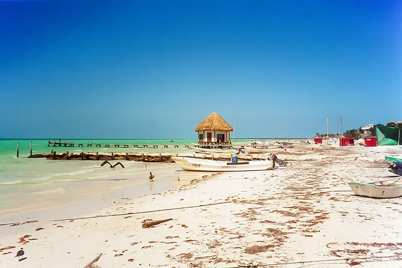 Historical photo of Isla Holbox beach in 2005 featuring traditional wooden boats and a rustic palm hut.