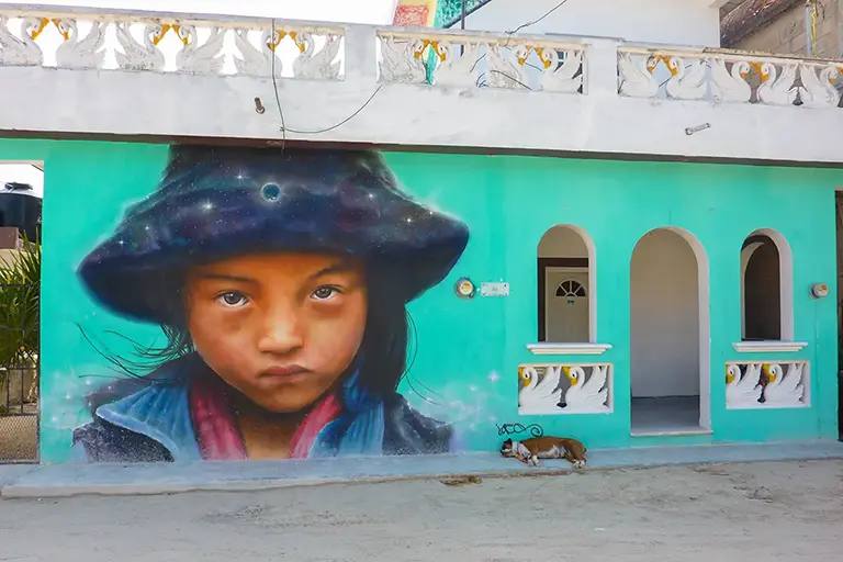 Kultiges Street-Art-Wandbild auf Isla Holbox, das einen Jungen mit Hut und Schal vor einem Sternenhimmel zeigt.