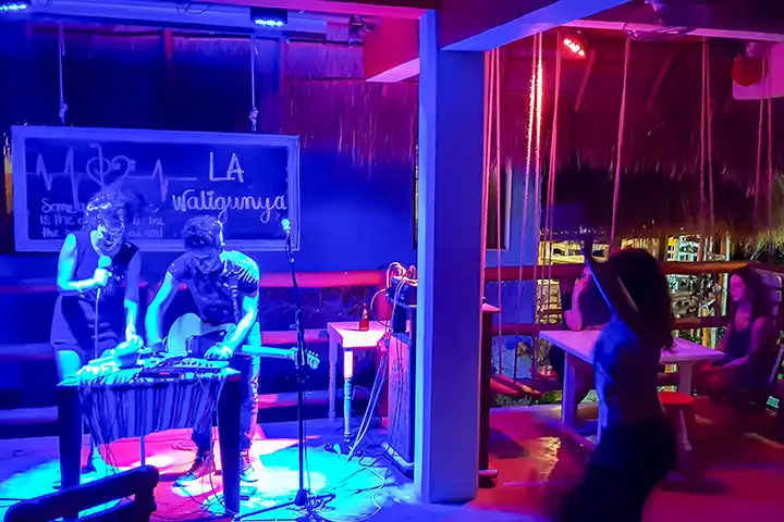 Two DJs performing under blue lights for dancers at the Tribu Bar in Holbox.