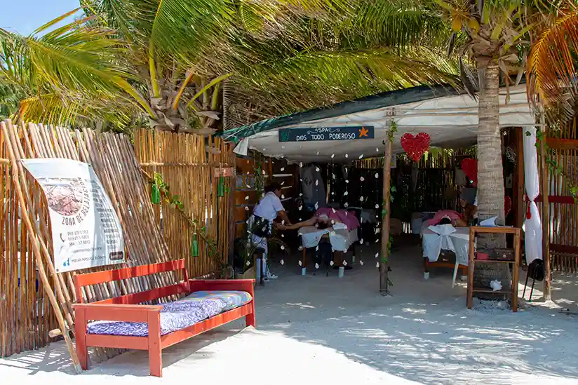 Inviting, open massage hut with two loungers and palm trees on Isla Holbox beach, ready for guests.