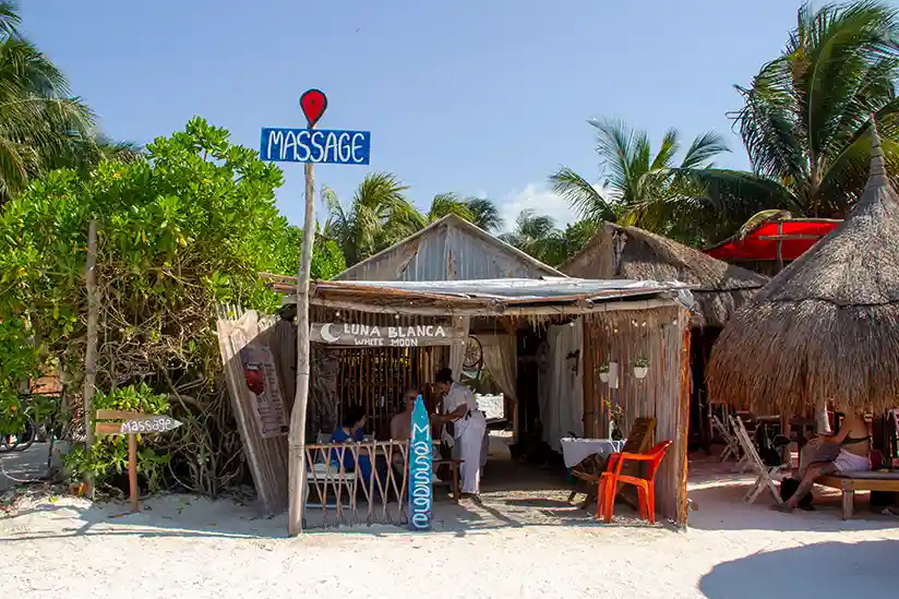 Simple wooden massage stand with a clear ‘MASSAGE’ sign right on Holbox's palm beach.