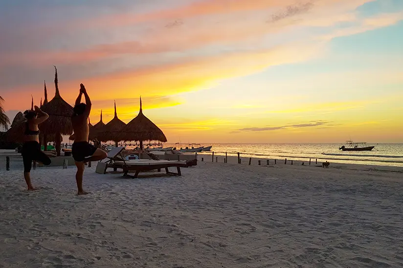 A group practices yoga poses on Holbox beach during a picturesque sunset.